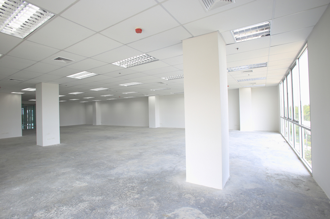 Leerer, unmöblierter Raum mit großen Fenstern, weißen Wänden und grauem Betonboden.